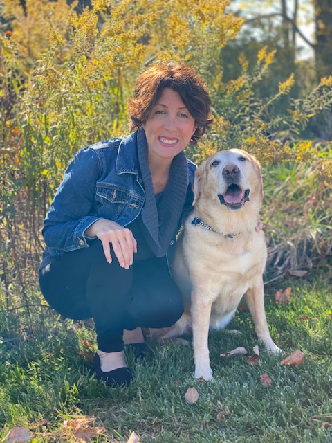 Kimberley crouching in a field of goldenrod with her certified guide dog, Ursula.